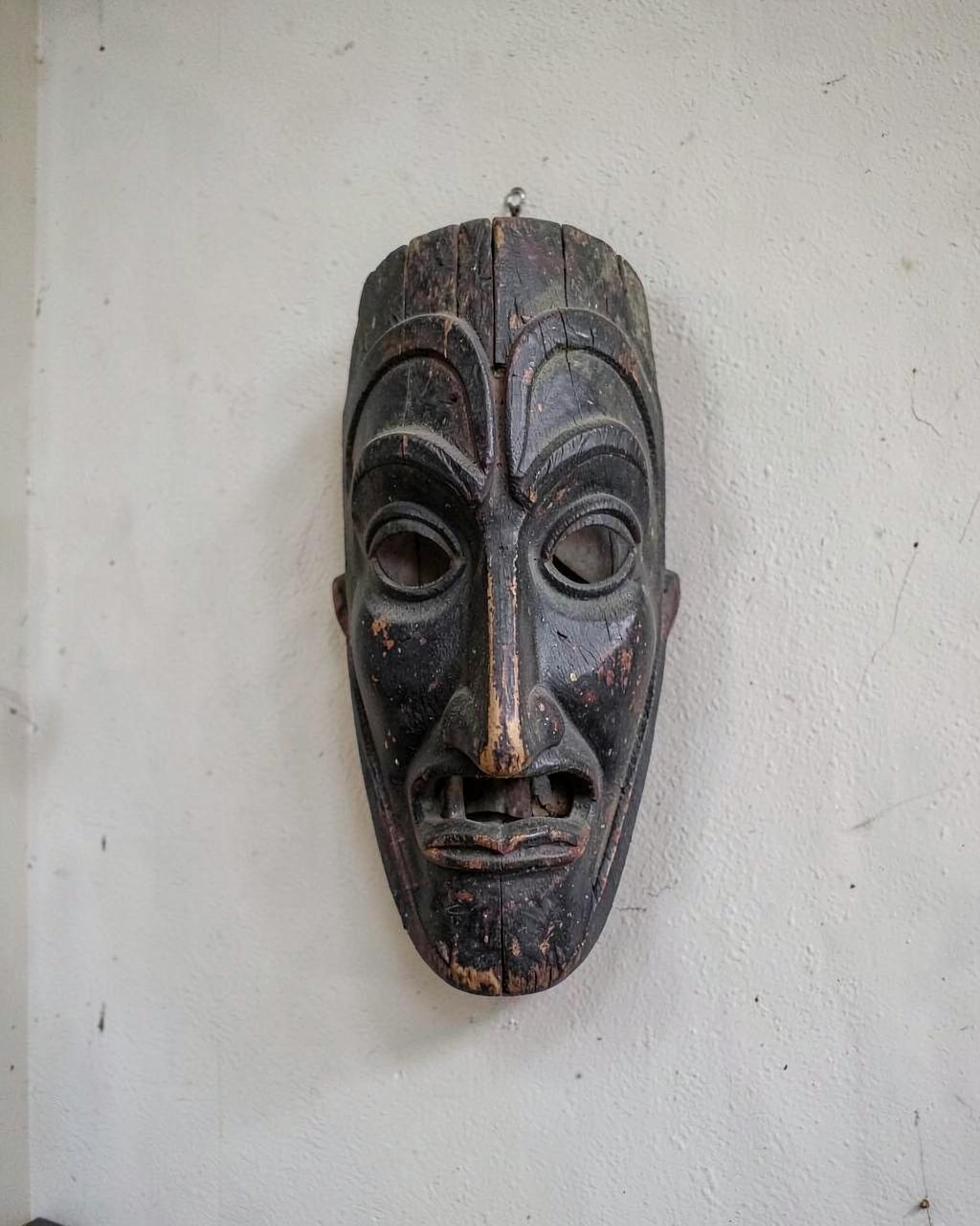 Foto demo: maschera in legno intagliato con patina scura appesa a una parete chiara