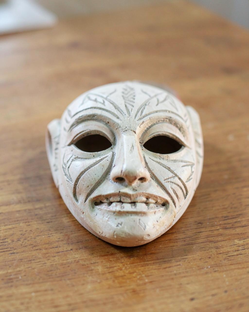 Foto demo: maschera in legno dipinta di chiaro con motivi incisi su un tavolo di legno